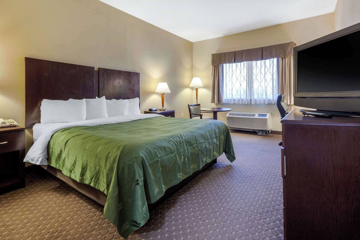A hotel room with a large bed, a desk with a chair, a flat-screen TV, and a window with curtains.