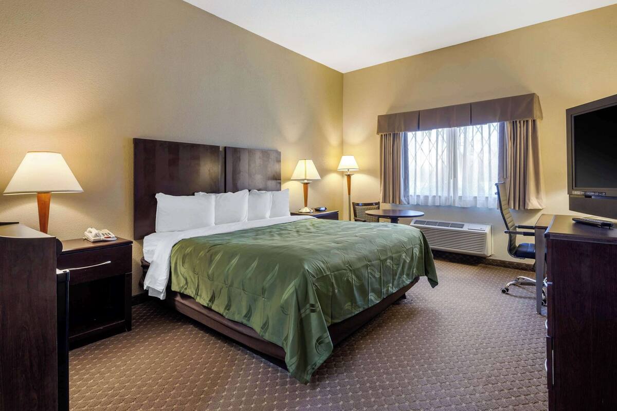 A hotel room with a large bed, two bedside lamps, a desk with a telephone, a chair, and a television.