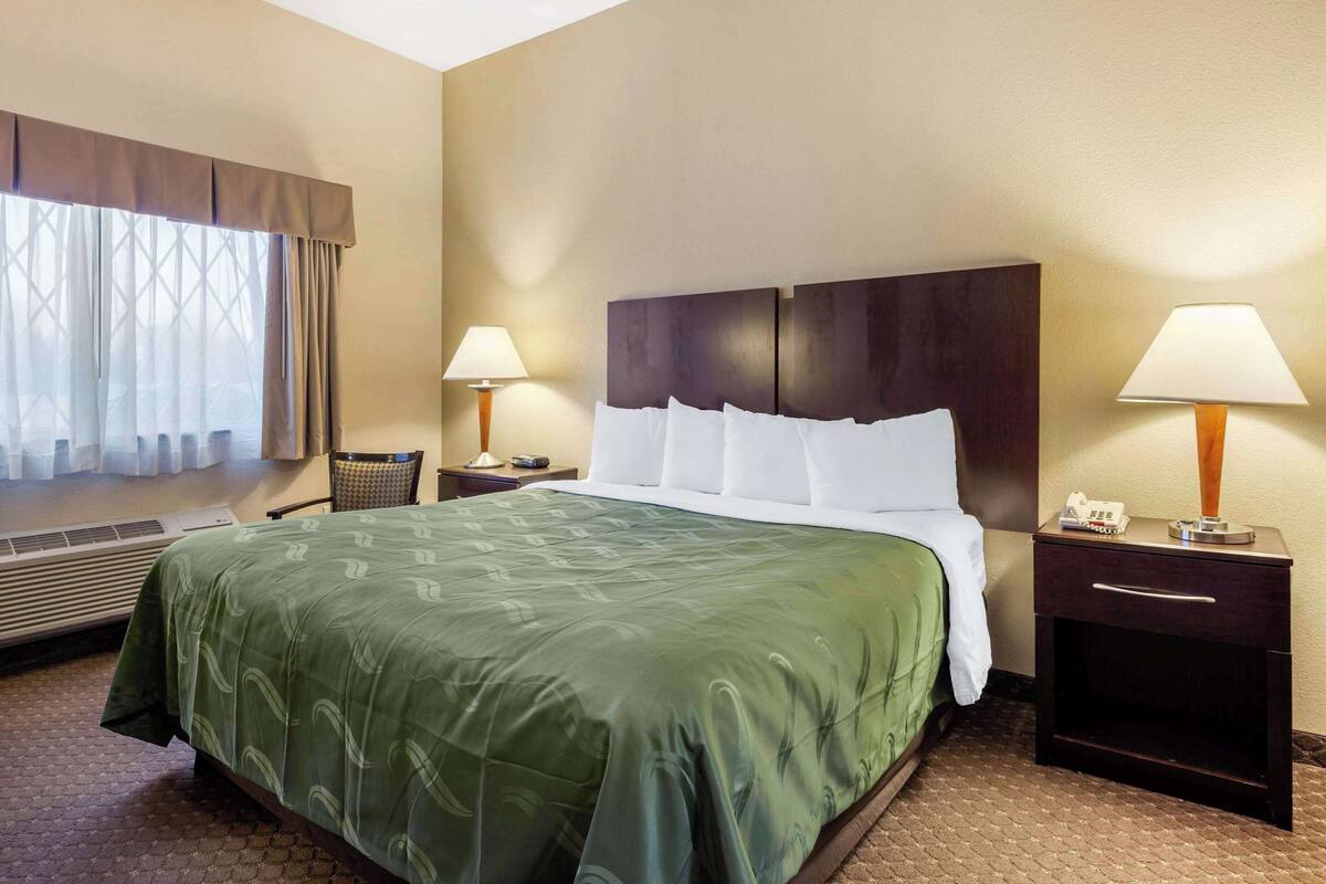 A hotel room with a large bed, two bedside tables with lamps, a chair, and a window with curtains.