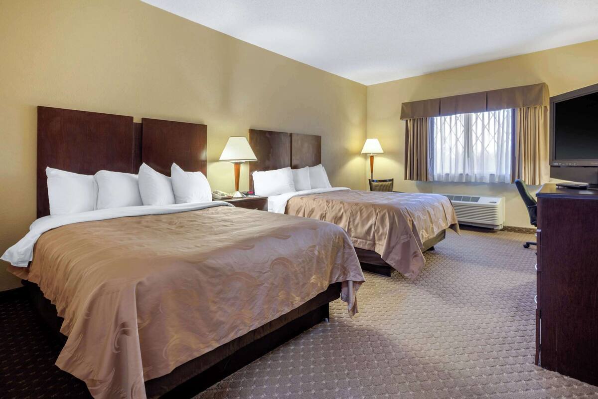 A hotel room with two beds, a TV, a desk, and a window with curtains.