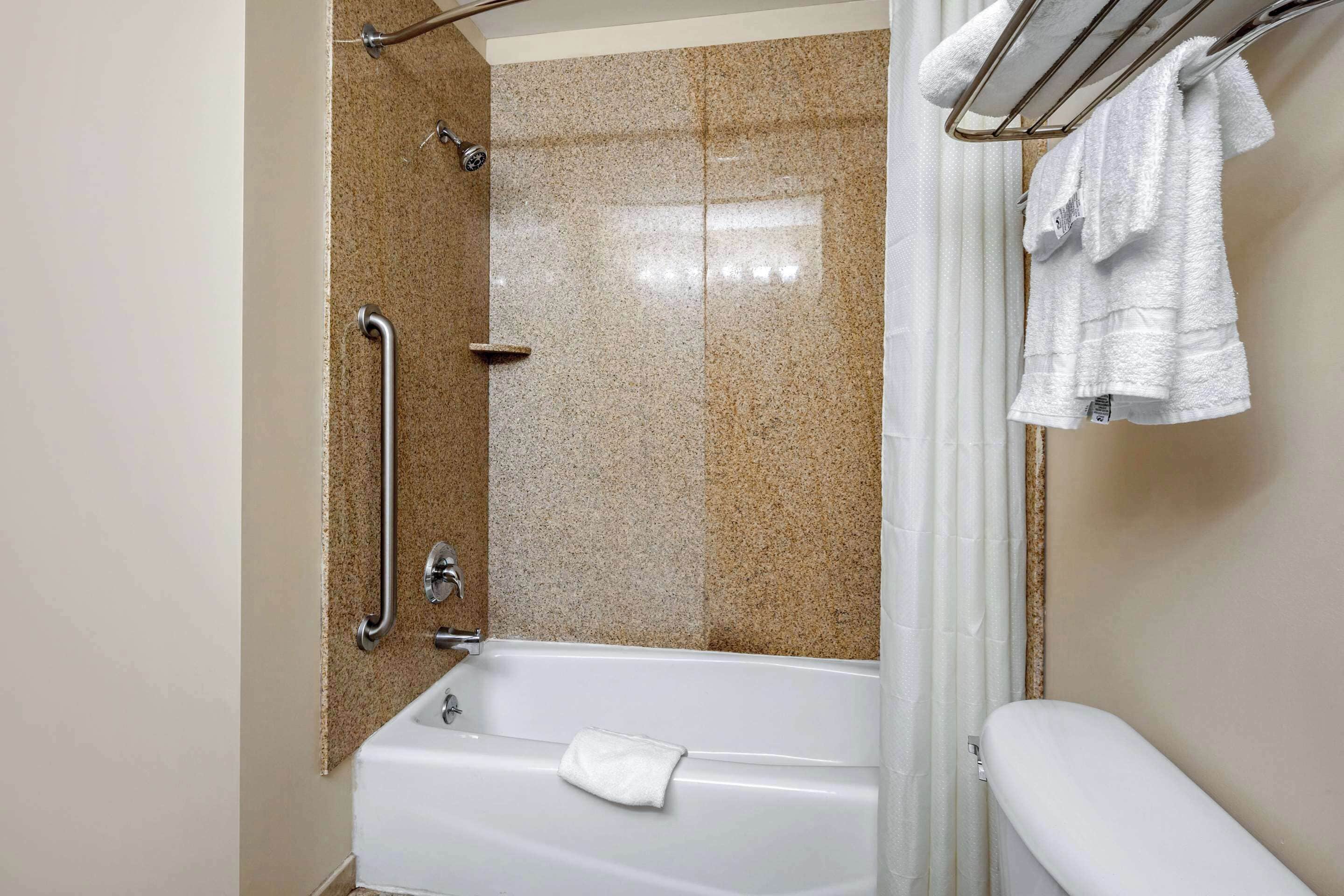 A bathroom with a shower, grab bars, a white bathtub, and a towel rack.