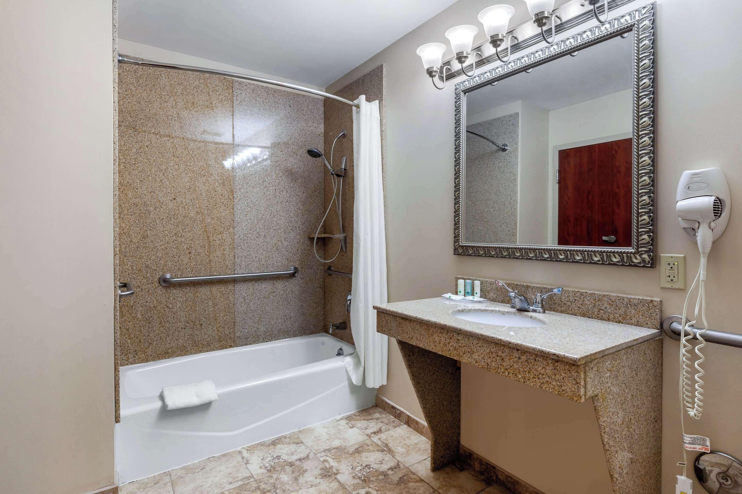 A bathroom with a shower, a bathtub, a vanity with a sink, a mirror, and a hairdryer.