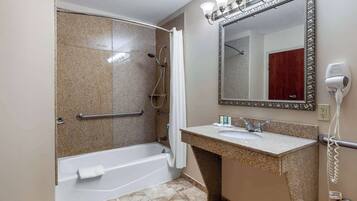 Un baño con ducha, bañera, tocador con lavabo, espejo y secador de pelo.