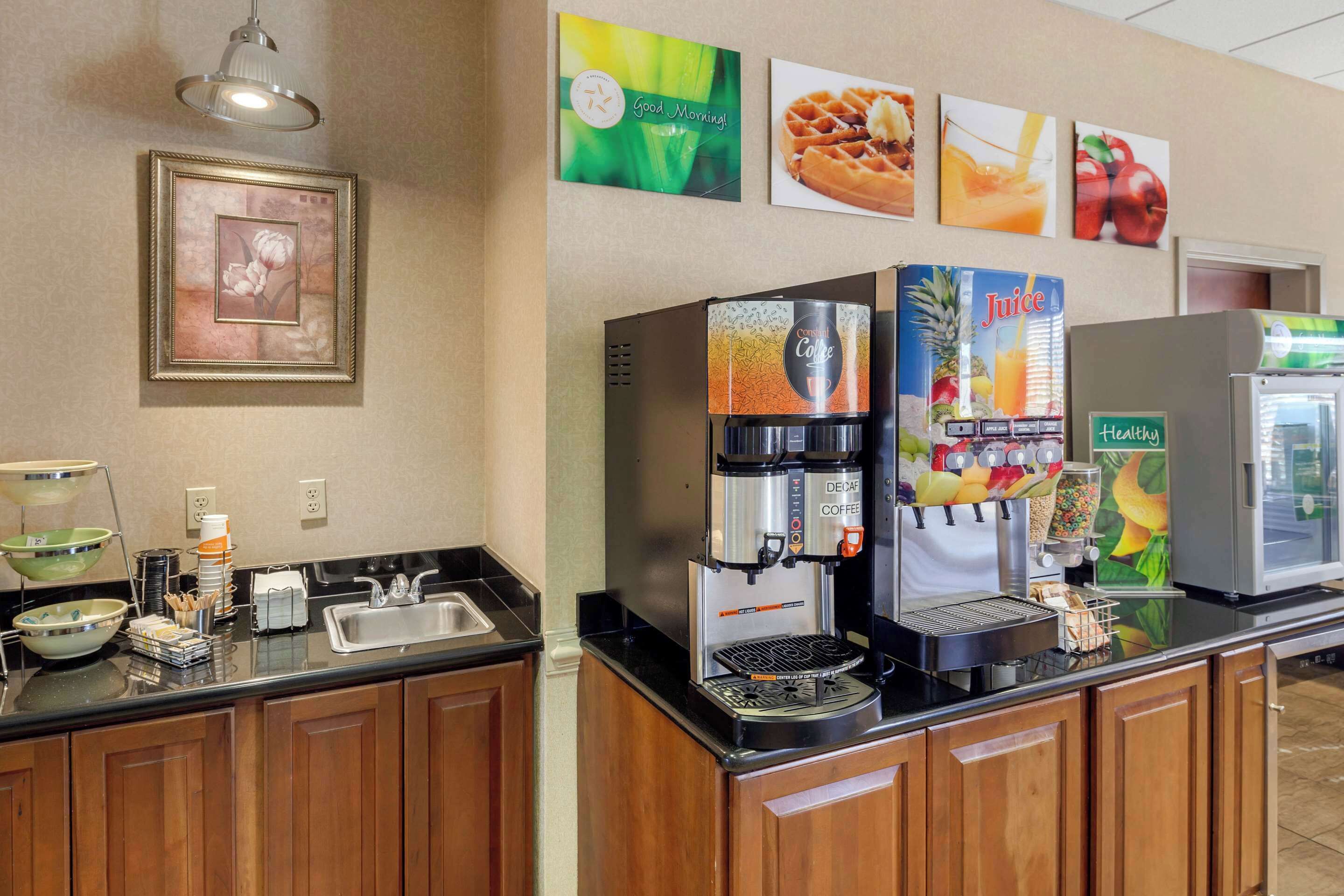 A coffee station with multiple beverage dispensers, a sink, and a refrigerated display.