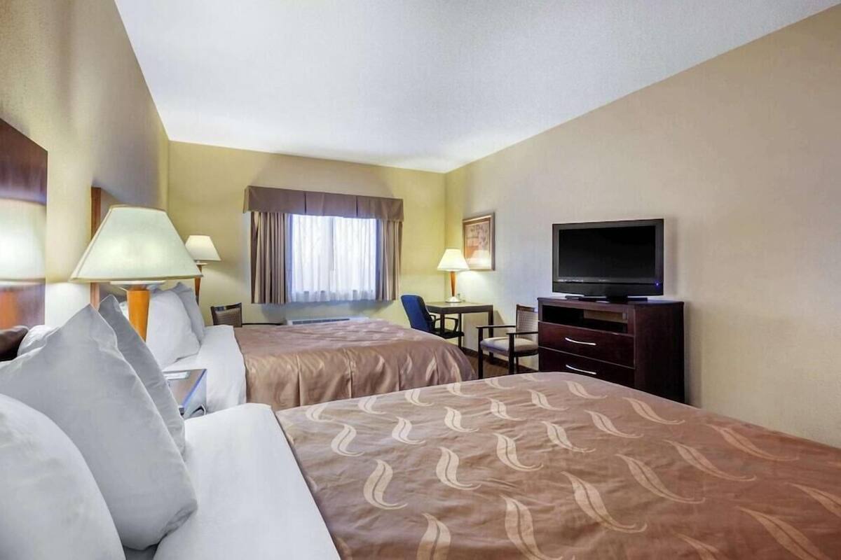 A hotel room with two beds, a desk, a chair, a television, and a window with curtains.