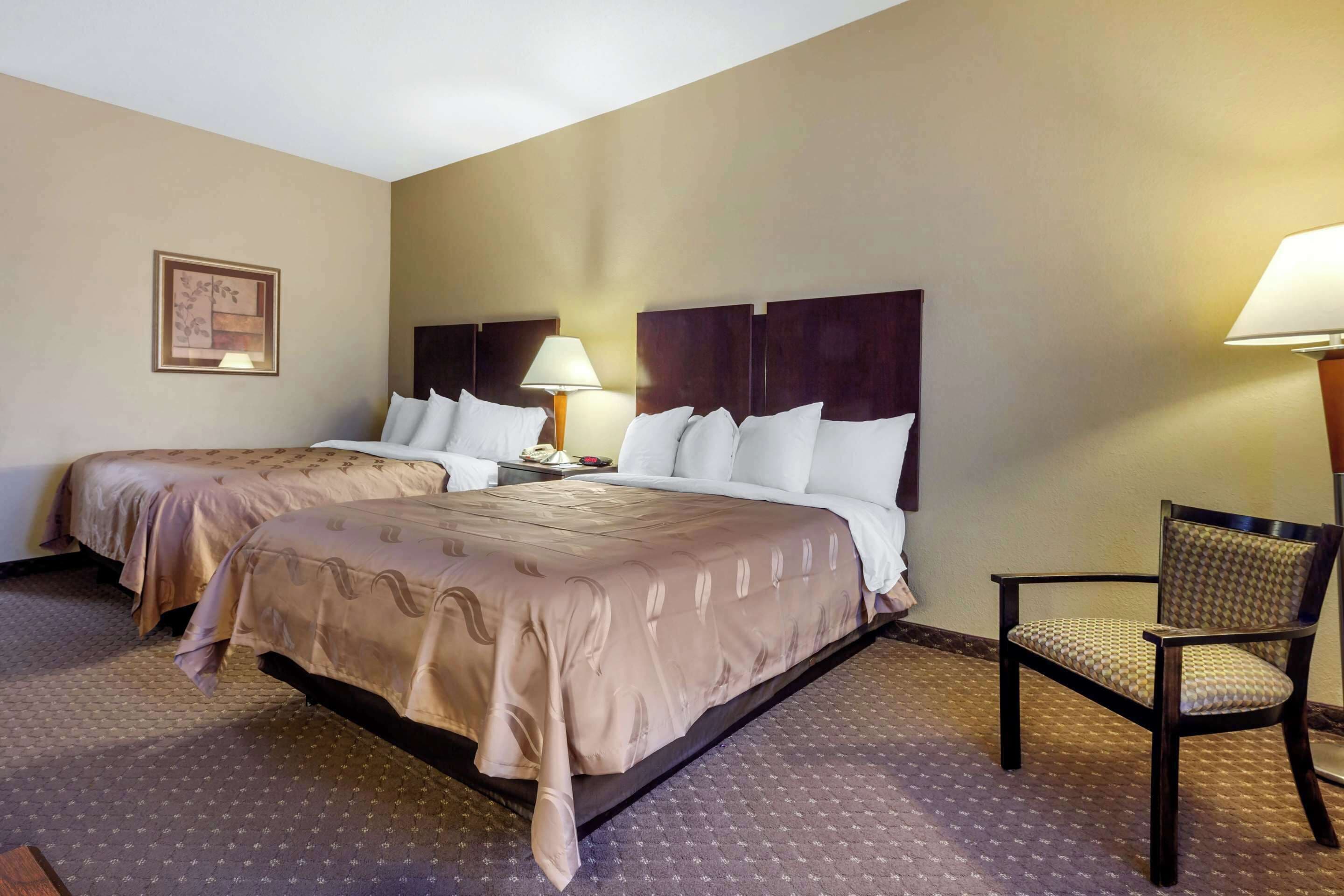 A hotel room with two beds, a chair, and a nightstand with a lamp.