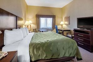 A hotel room with a large bed, a desk with a chair, a television, and a window with curtains.