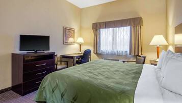 Habitación de hotel con cama, escritorio, silla, televisor y ventana con cortinas.