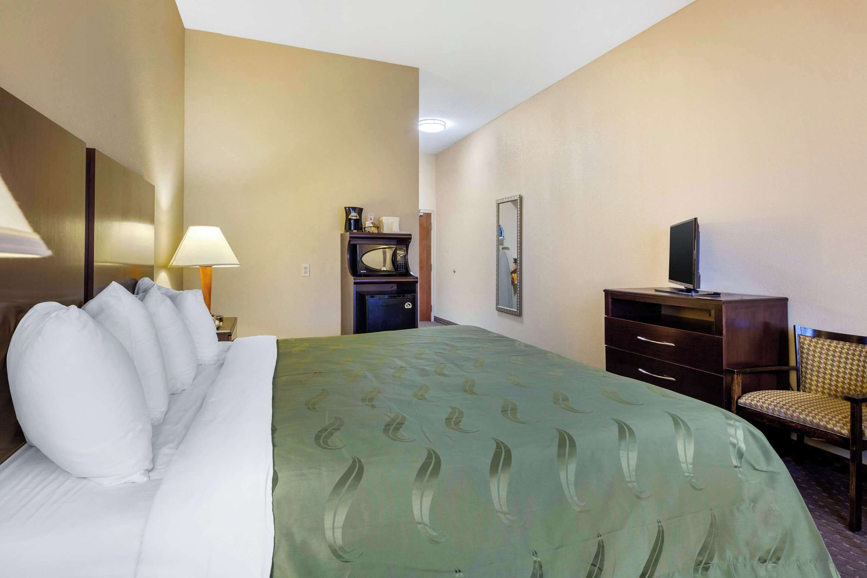 A hotel room with a large bed, a desk with a computer, a chair, a television, and a microwave.