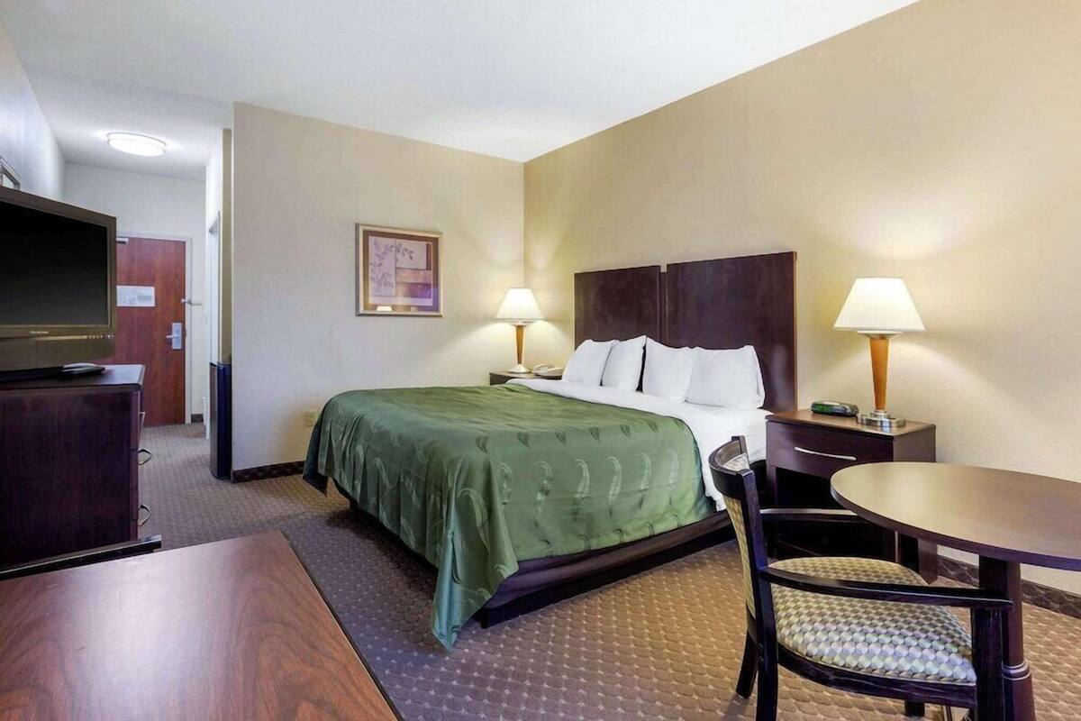 A hotel room with a bed, two bedside lamps, a television, a desk, and a chair.