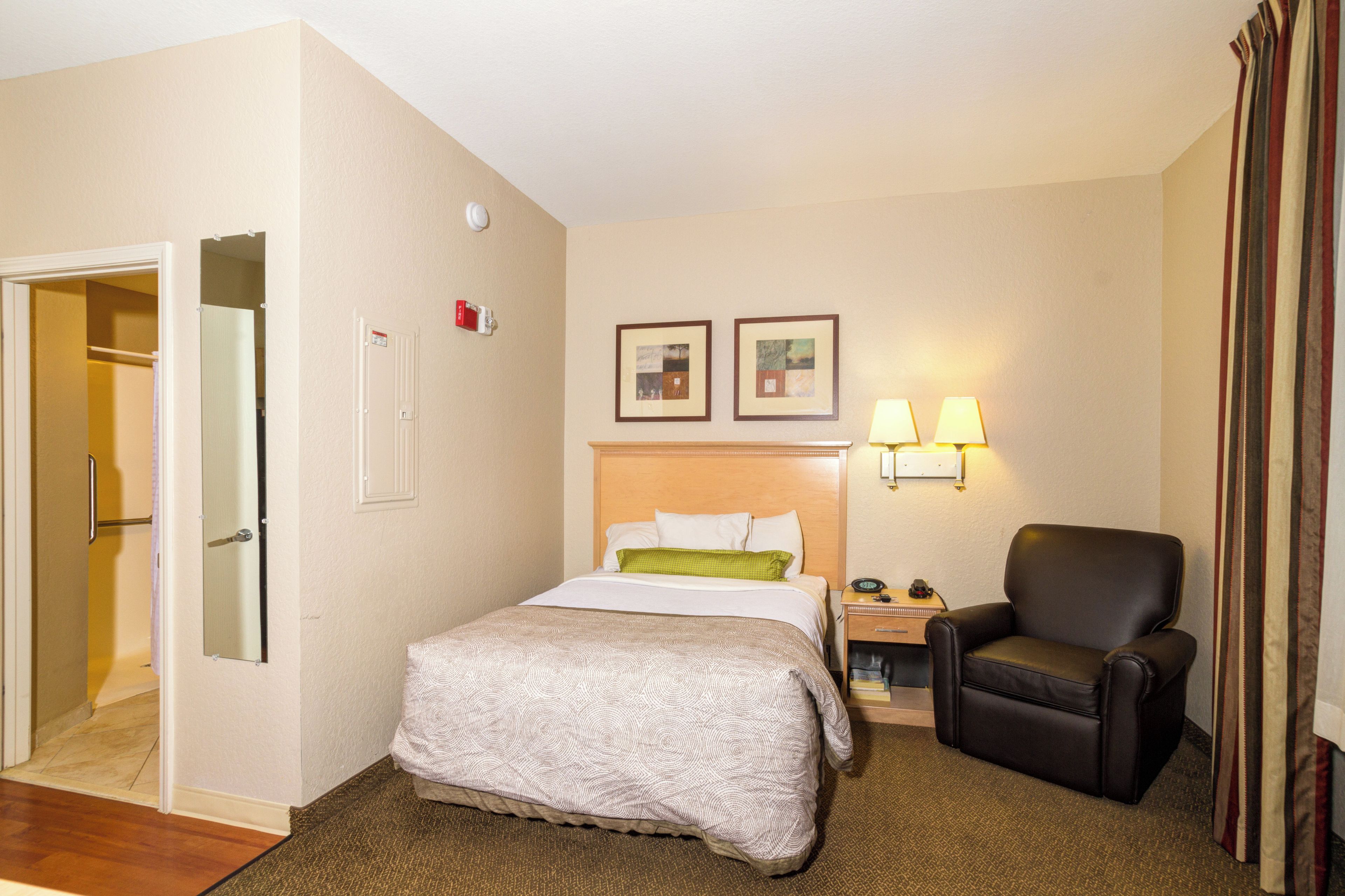 A hotel room with a bed, a chair, a nightstand, and a door leading to a bathroom.