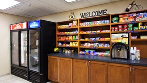 Un bar de aperitivos con un cartel de 'Welcome', un refrigerador y estantes llenos de diversos bocadillos y bebidas.
