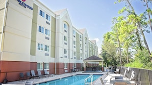 Un hotel con piscina, mobiliario exterior y un patio cubierto.