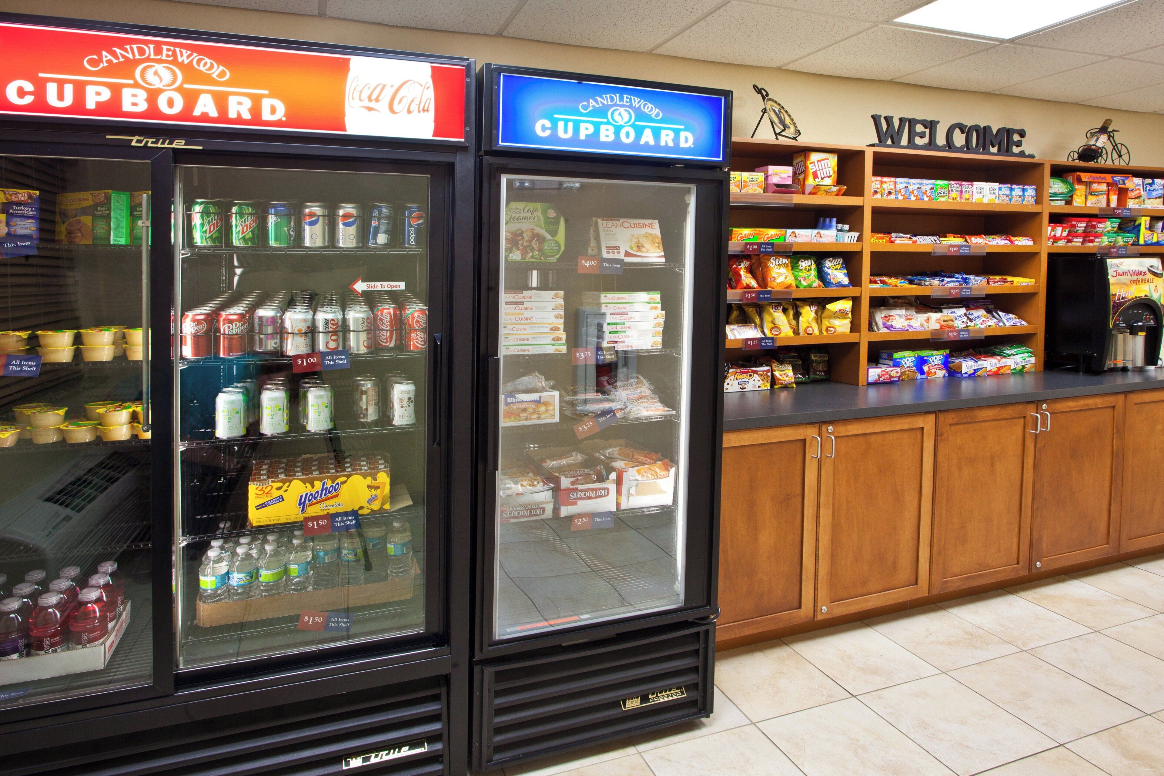 A beverage cooler with various drinks and snacks, a 'Welcome' sign, and shelves stocked with snacks.