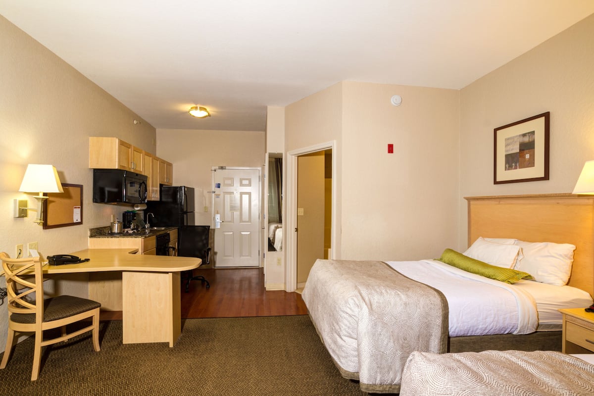 Une chambre d’hôtel comprenant un lit, un bureau, une chaise, une kitchenette et une porte donnant sur une autre pièce.
