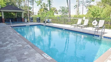 A rectangular swimming pool with a tiled deck, a gazebo, and lounge chairs.