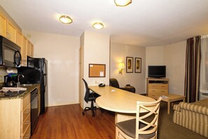 Een compacte hotelkamer met een kitchenette, een eettafel met stoelen, een televisie en een bank.