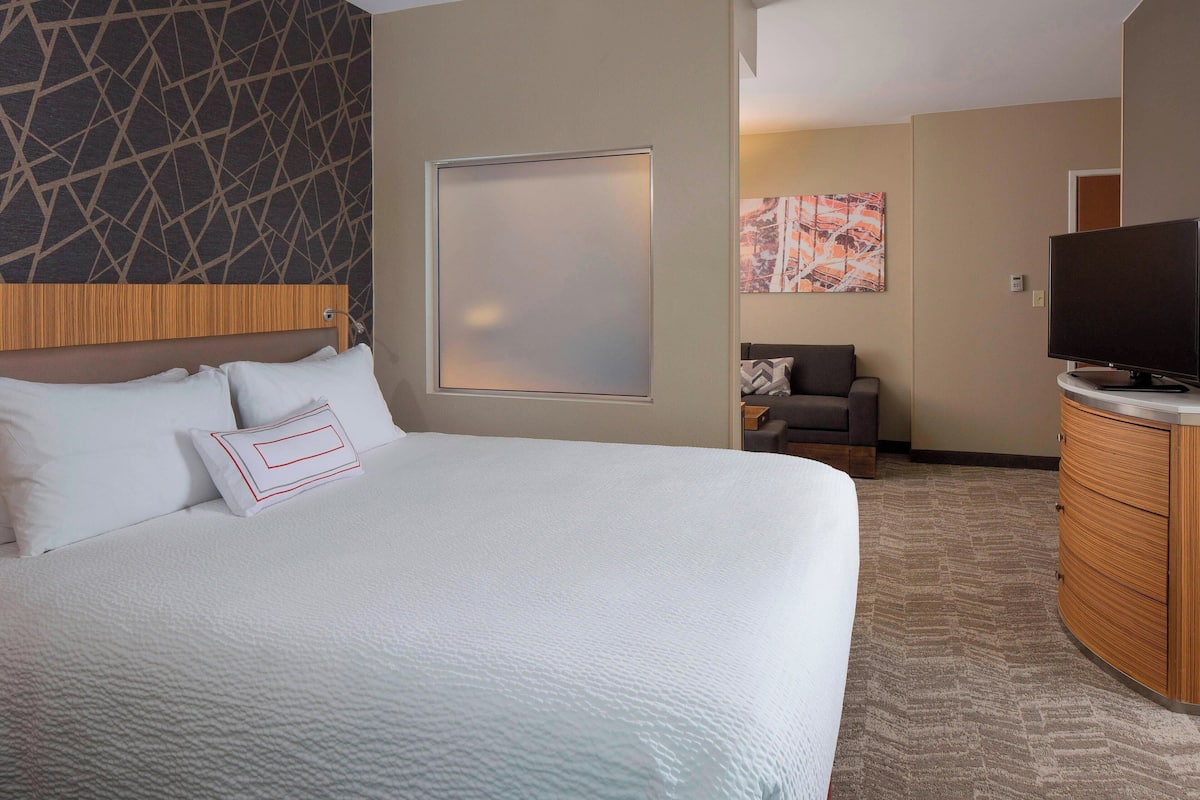 Habitación de hotel con una cama grande, cabecera de madera, televisor, escritorio y una silla.