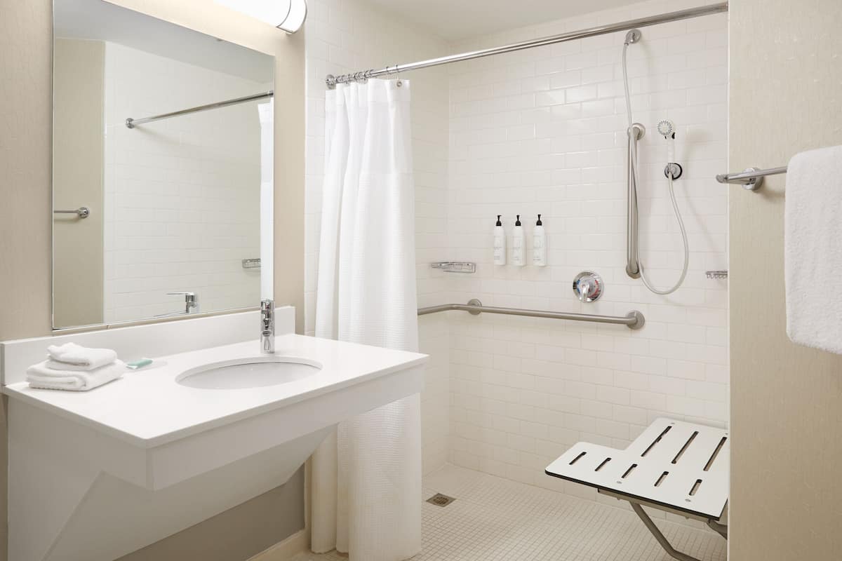 Un baño moderno con lavamanos, espejo y zona de ducha blancos.