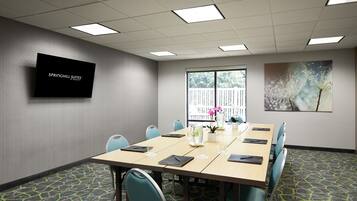 A conference room with a long table, chairs, a TV screen, a window with a view, and a patterned carpet.