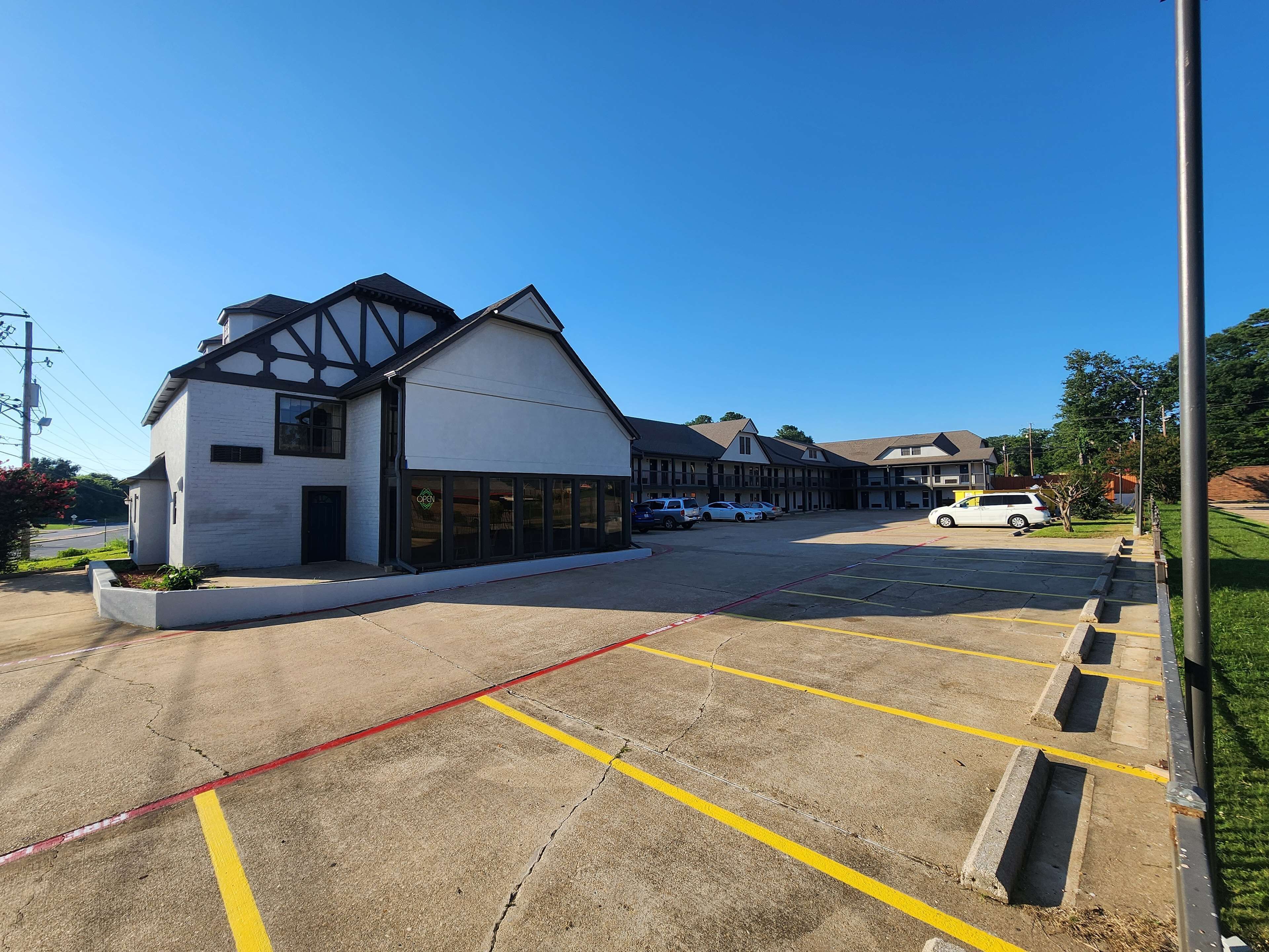 A building with a white facade and dark trim, a parking lot with yellow lines, and several parked cars.