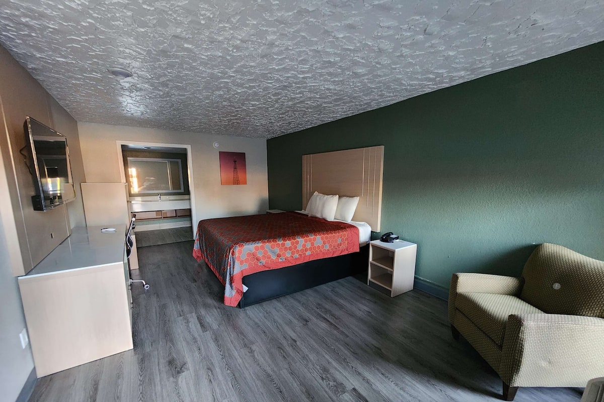 A hotel room with a bed, a chair, a bedside table, a desk, and a mirror.