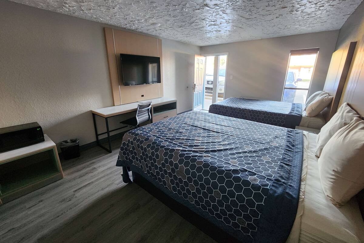 A hotel room with a large bed, a desk with a flat-screen TV, a chair, and a window with a view of the outside.