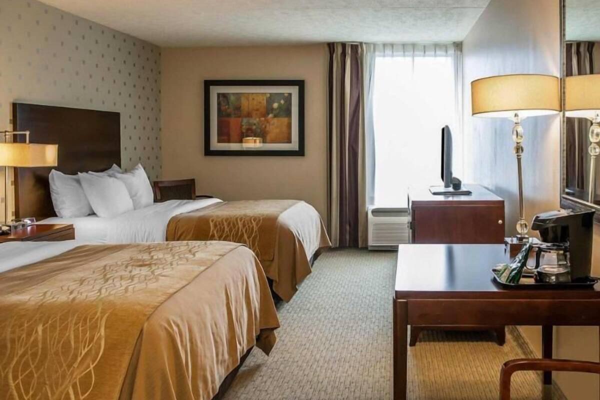 A hotel room with two beds, a desk, a television, a coffee maker, and a framed picture on the wall.