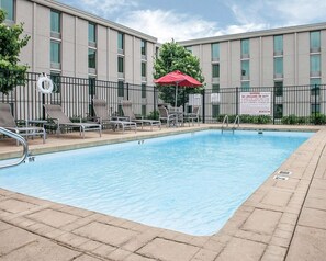 A rectangular pool with a metal ladder and a red umbrella. There are lounge chairs and a sign warning about no lifeguard duty.