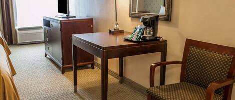 A hotel room with a wooden desk, a chair, a television, a lamp, and a mirror.
