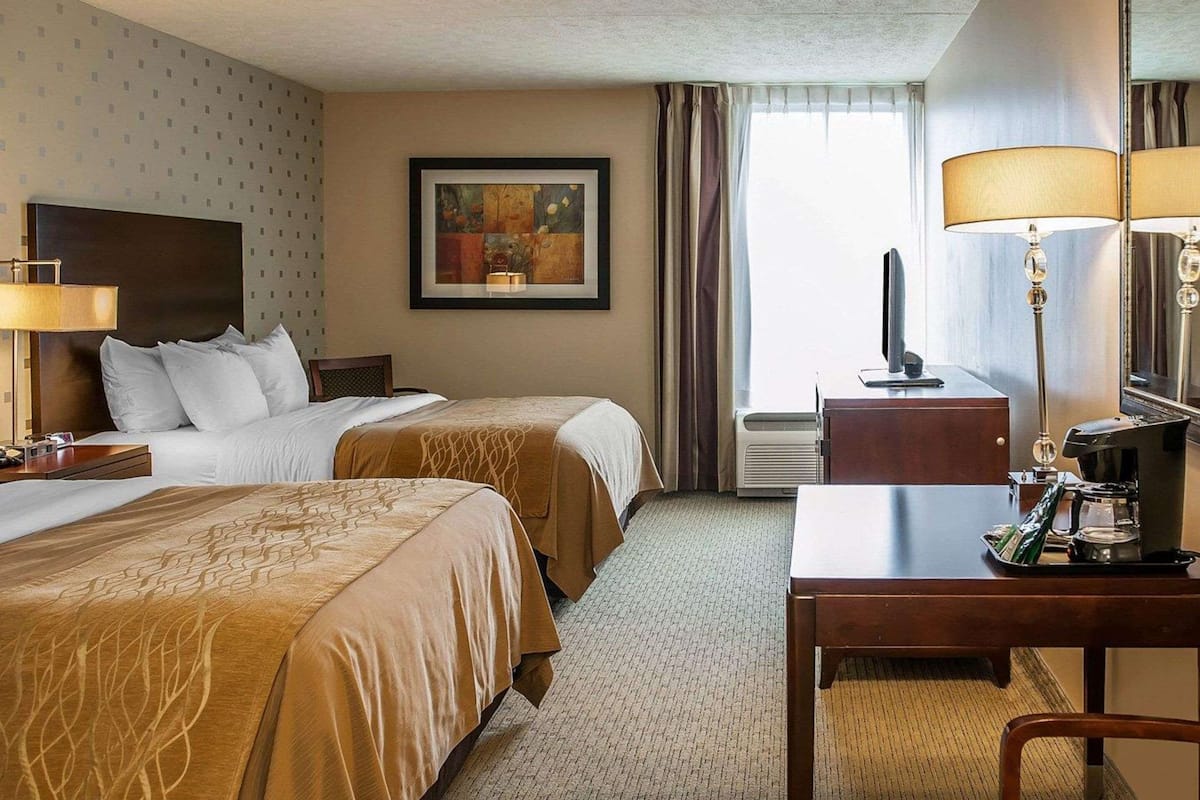 A hotel room with two beds, a desk, a coffee maker, a TV, and a painting on the wall.