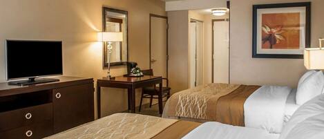 A hotel room with two beds, a desk with a lamp, a television, and a framed picture on the wall.