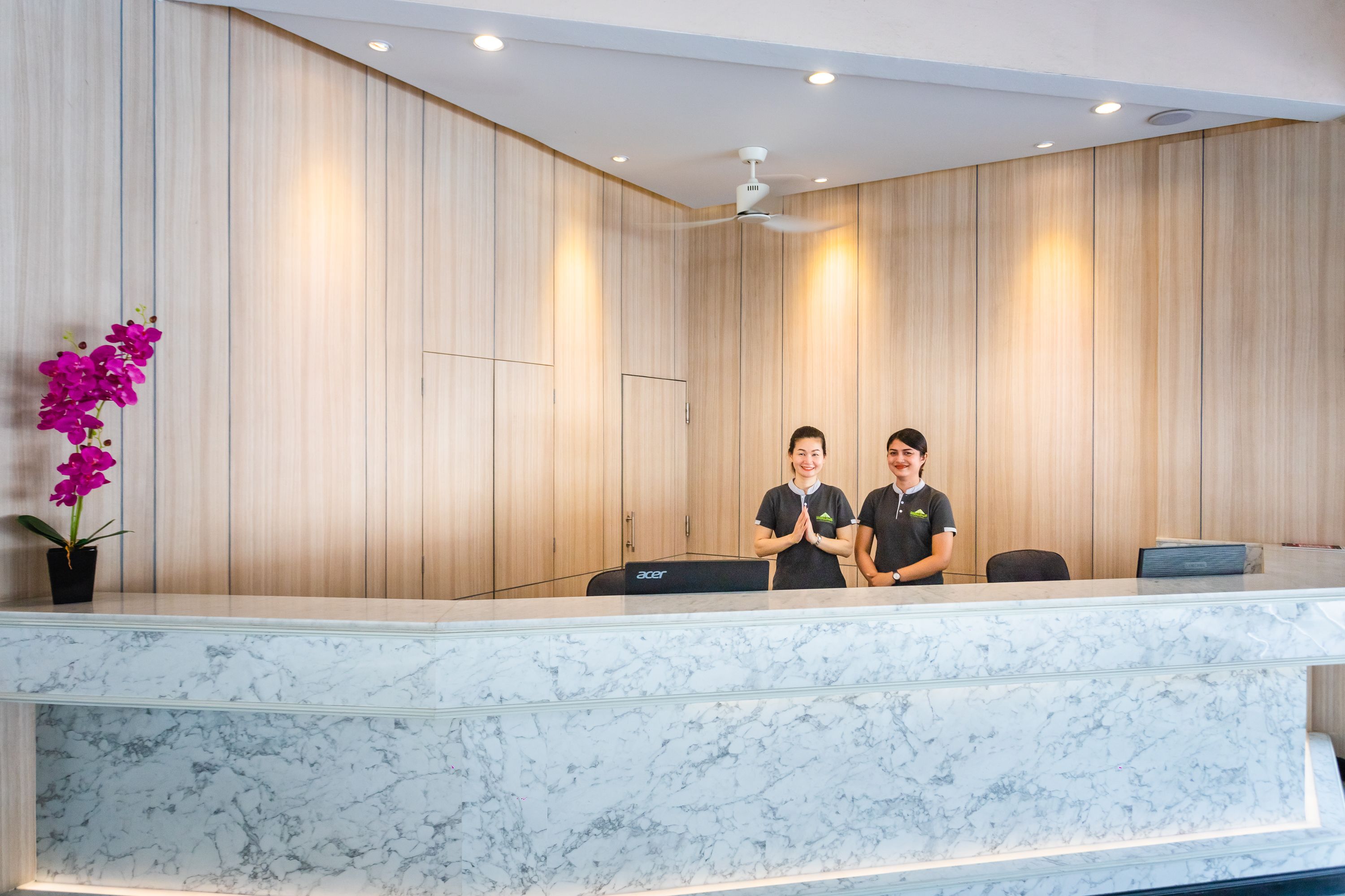 A reception desk with a marble top, wooden panel walls, and a ceiling fan.