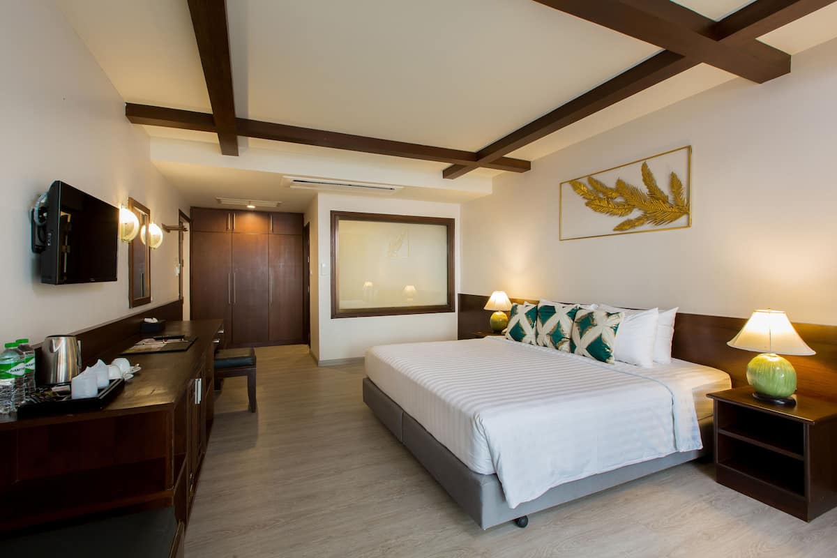 Una habitación de hotel con cama, mesita de noche, lámpara, televisor, escritorio y un ventanal grande.