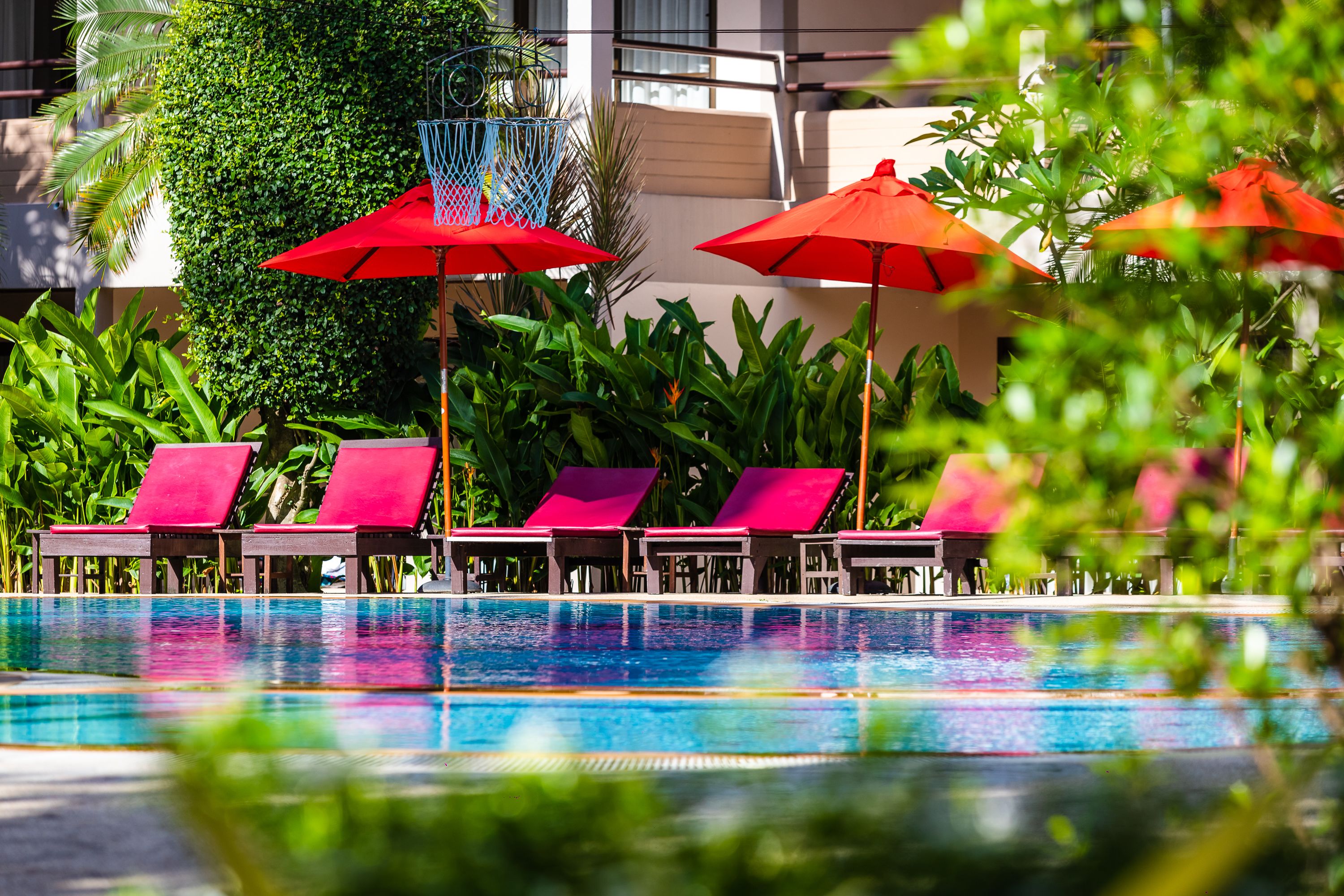 A poolside area with red umbrellas, pink lounge chairs, and a clear pool.