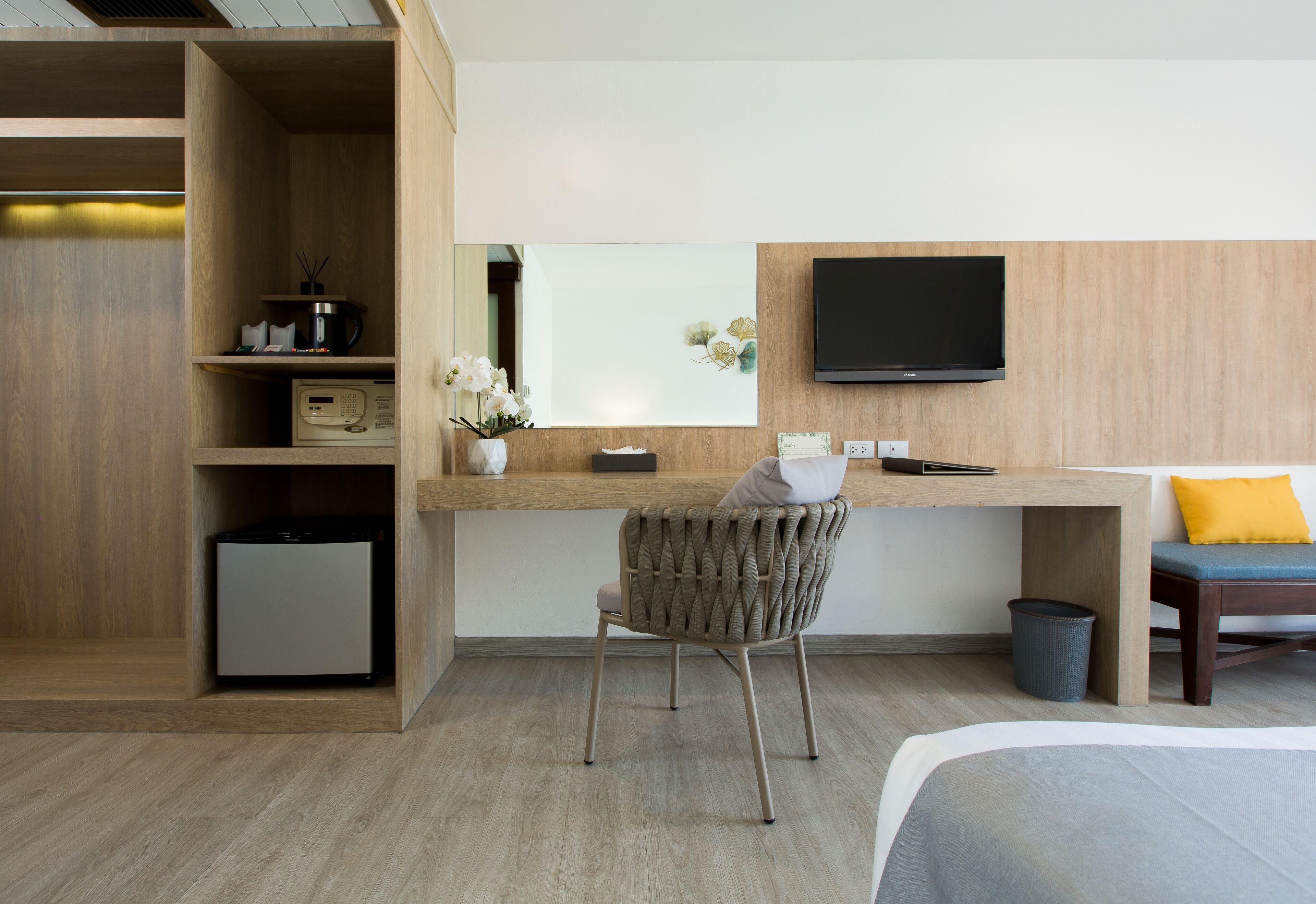 A hotel room with a wooden desk, a television, a chair, a bed, and a small refrigerator.