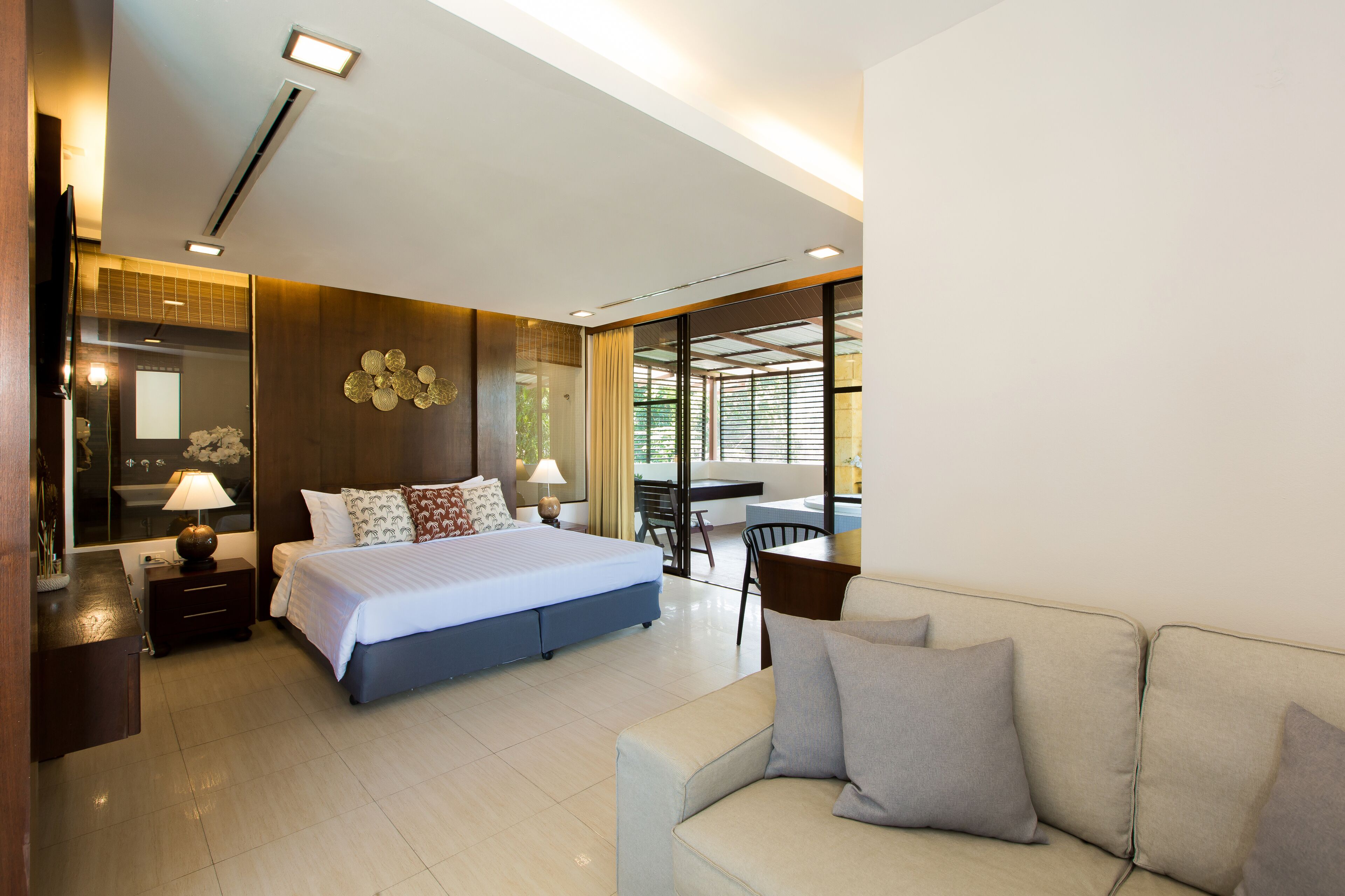A modern hotel room with a large bed, a sofa, a desk, and a balcony with a view.