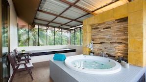 A modern bathroom with a stone wall, a bathtub, and a seating area with a table and chairs. - Coconut Village Resort (Patong)
