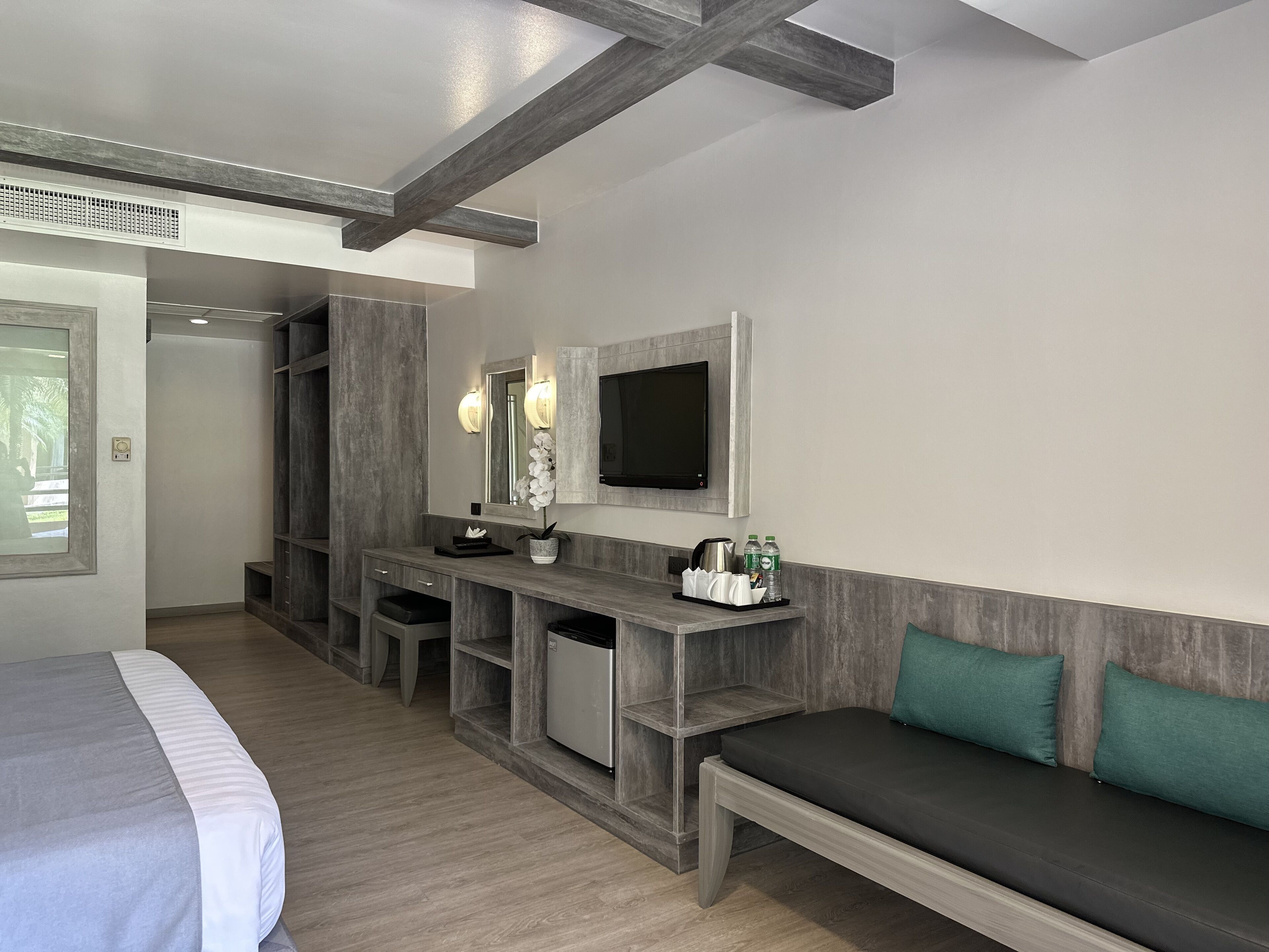 A modern hotel room with a bed, a desk with a computer, a TV, and a seating area with cushions.