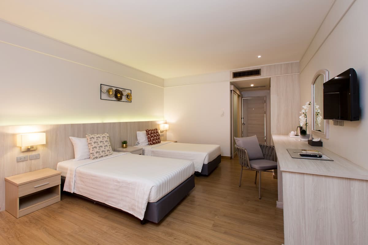 Habitación de hotel con dos camas, un escritorio, una silla, un televisor y una puerta que da a otra habitación.