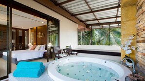 A hotel room with a large bathtub, a bed, a seating area, and a view of greenery outside. - Coconut Village Resort (Patong)