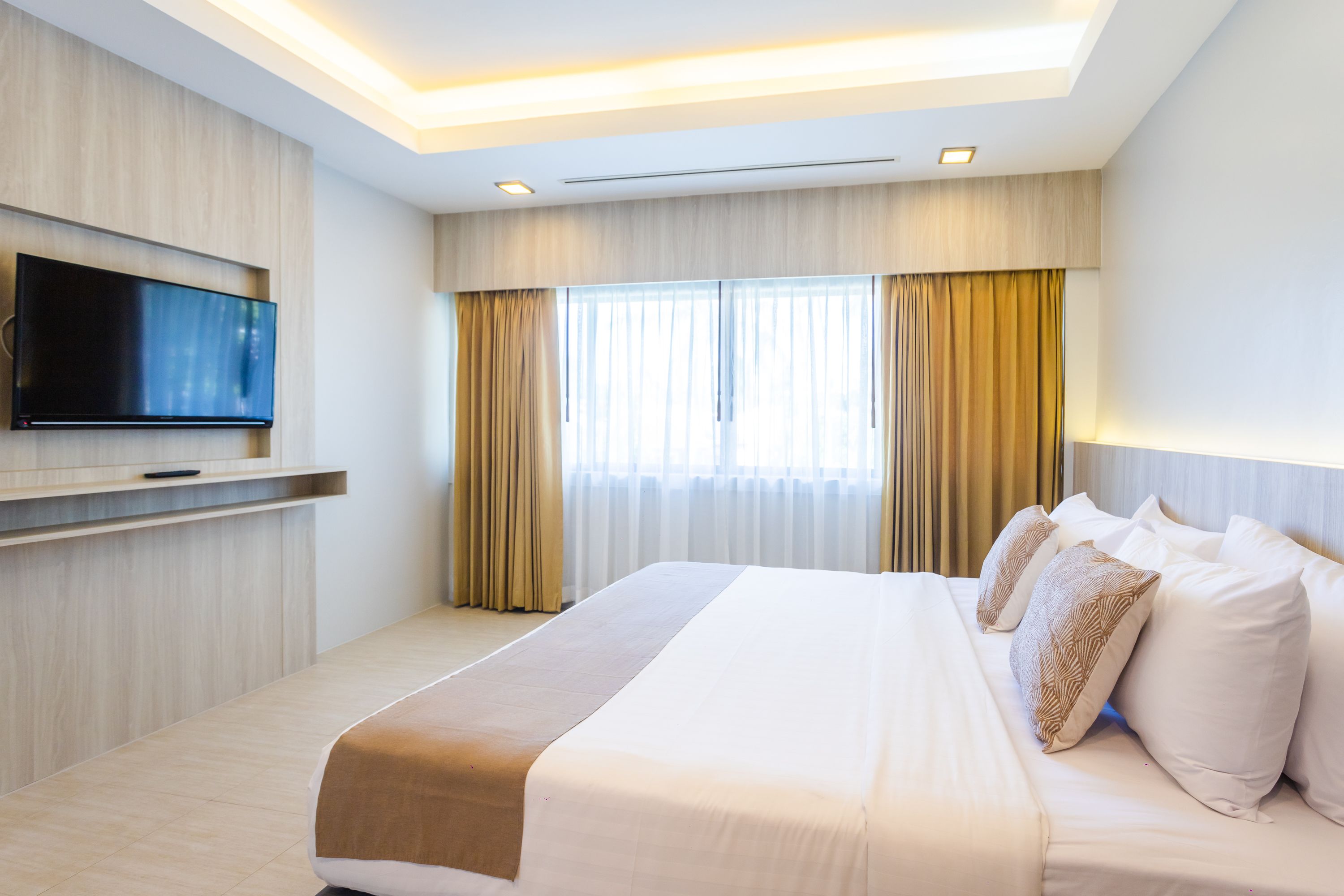 A hotel room with a large bed, a flat-screen TV mounted on the wall, and a window with curtains.