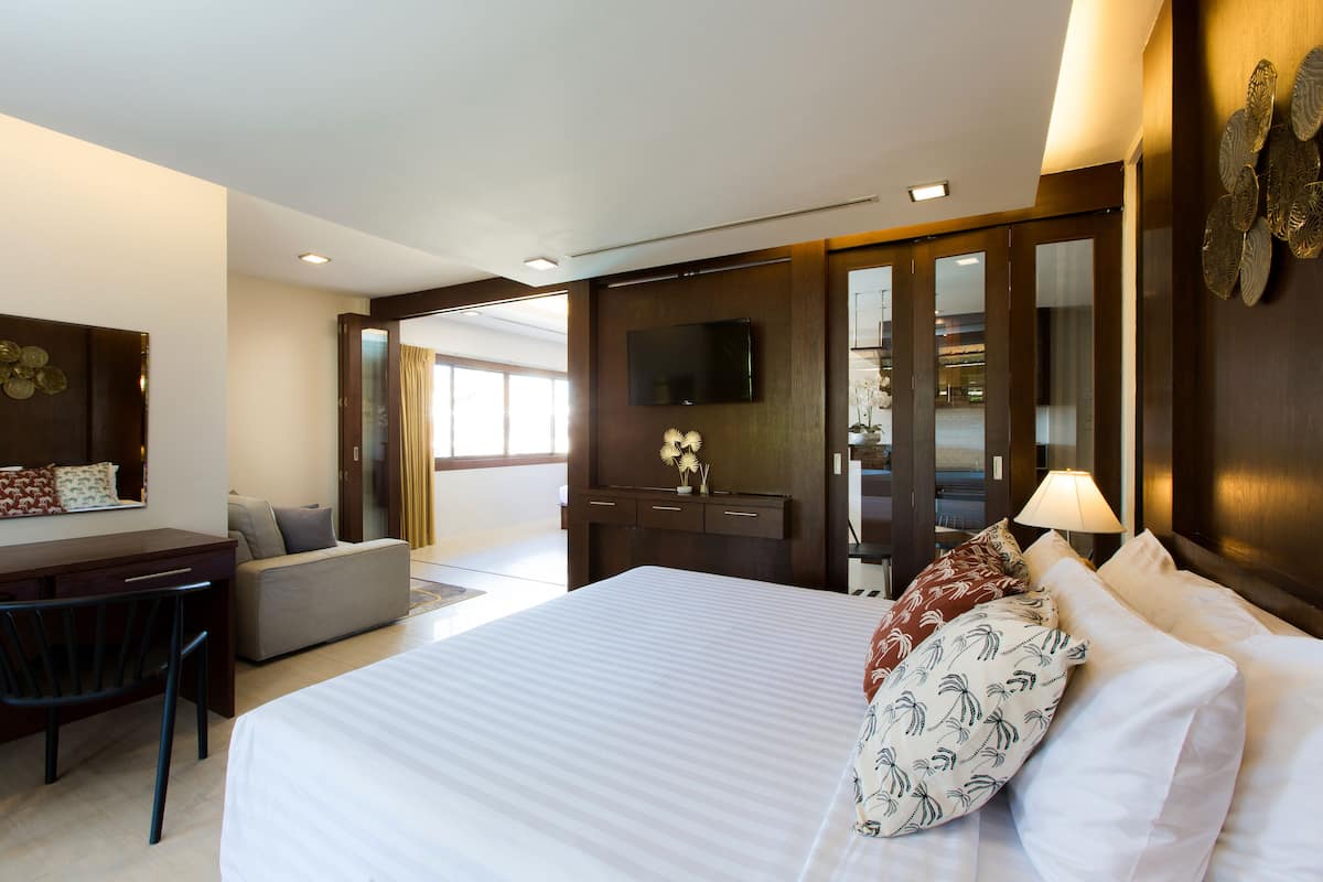 Habitación de hotel con una cama grande, un escritorio, un sofá, un televisor y un baño visible a través de una puerta abierta.