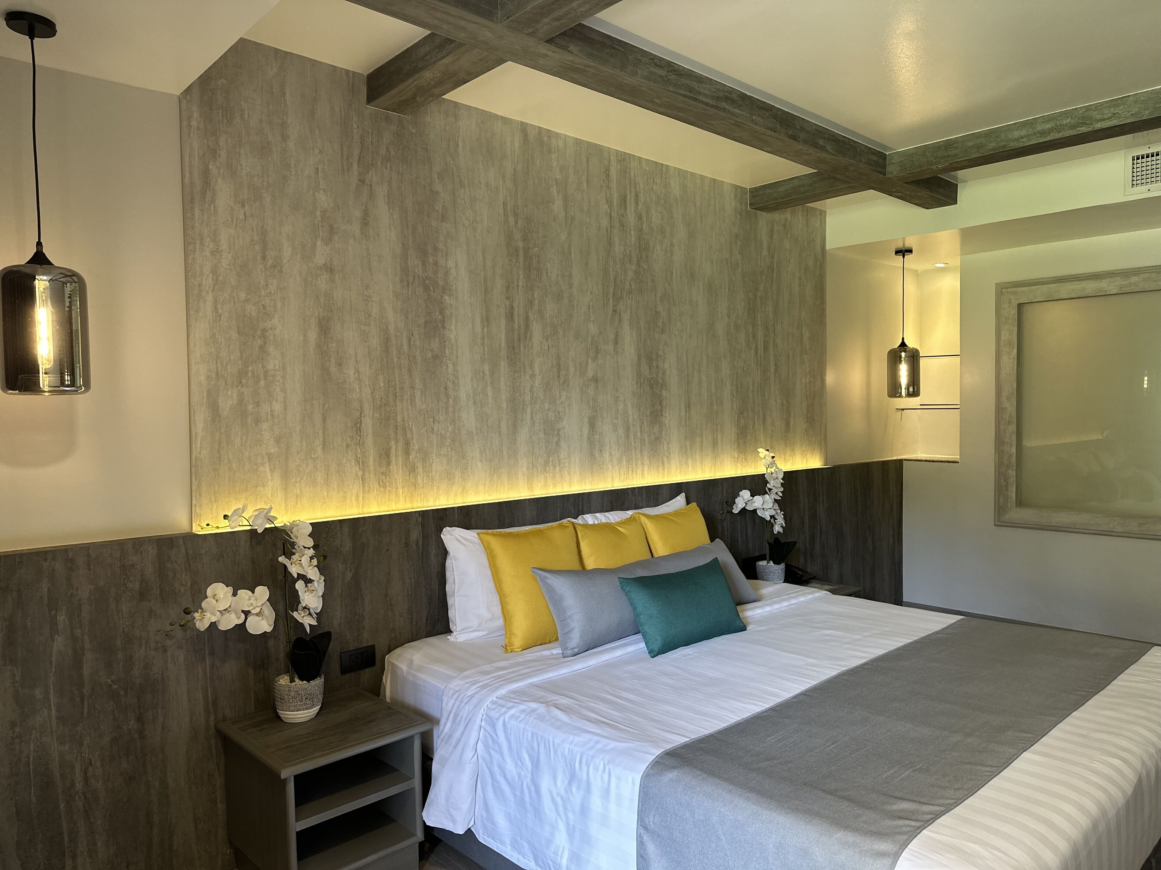 A modern bedroom with a large bed, wooden beams, and pendant lighting.