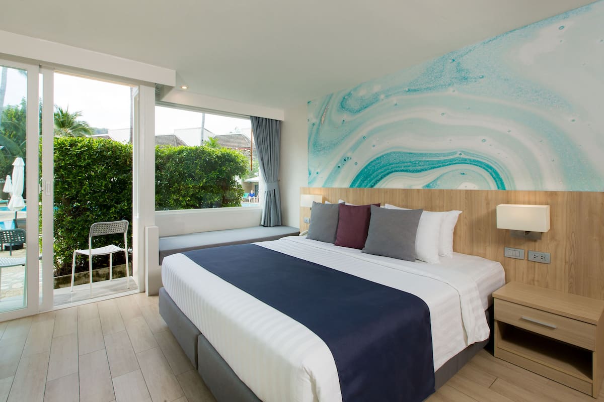 Habitación de hotel con una cama grande, cabecera de madera, mesita de noche y vistas al exterior.
