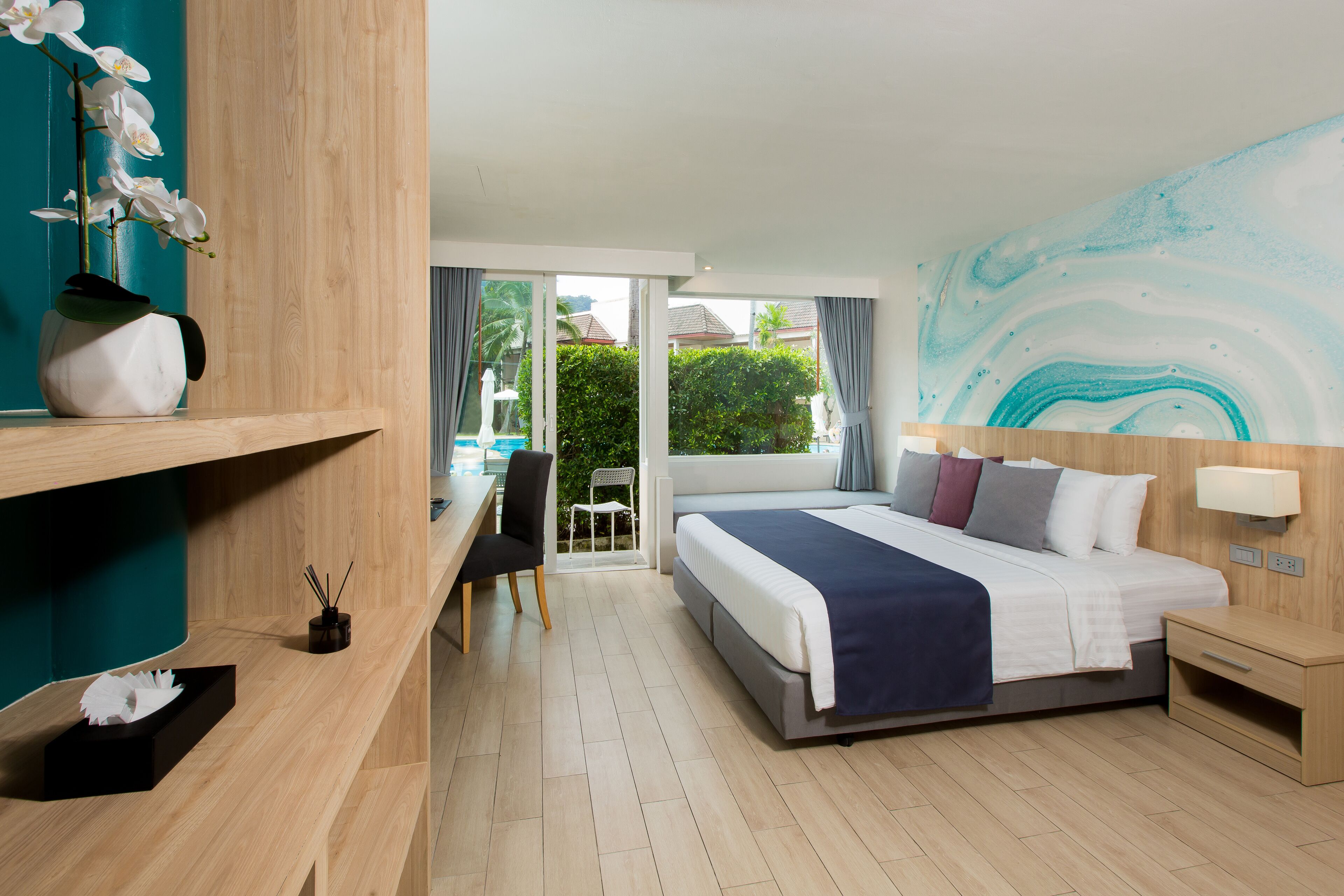 A hotel room with a bed, a desk, a chair, a small table, and a wall with a painting.