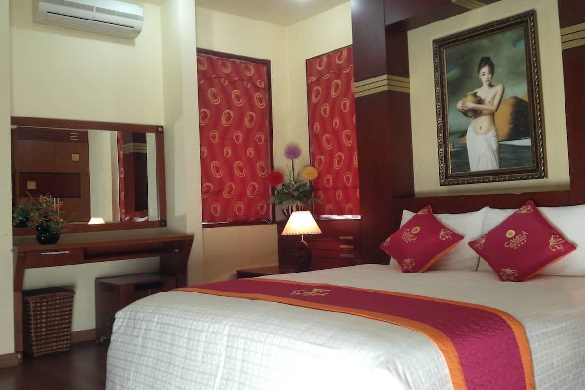 Une chambre d’hôtel avec un lit, un bureau, un miroir, une lampe et un tableau au mur.