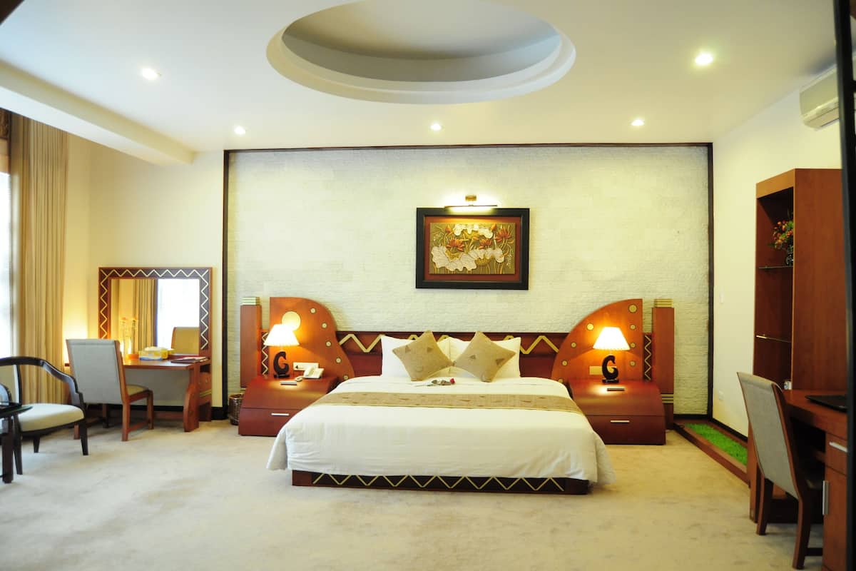 Une chambre d’hôtel avec un grand lit, deux tables de chevet avec des lampes, un bureau avec une chaise et un tableau encadré au mur.