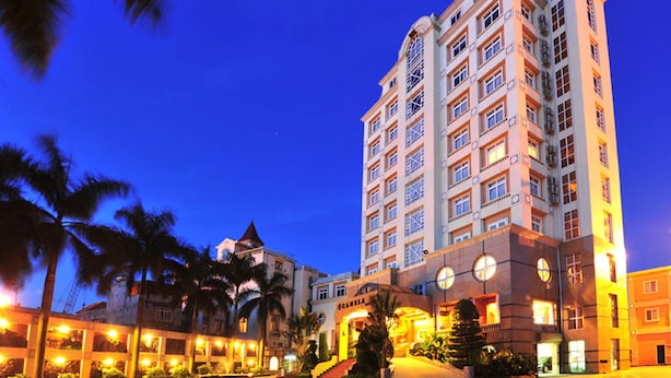 A multi-story hotel with a central entrance, palm trees, and a well-lit facade. - Camela Hotel & Resort (Hai Phong)
