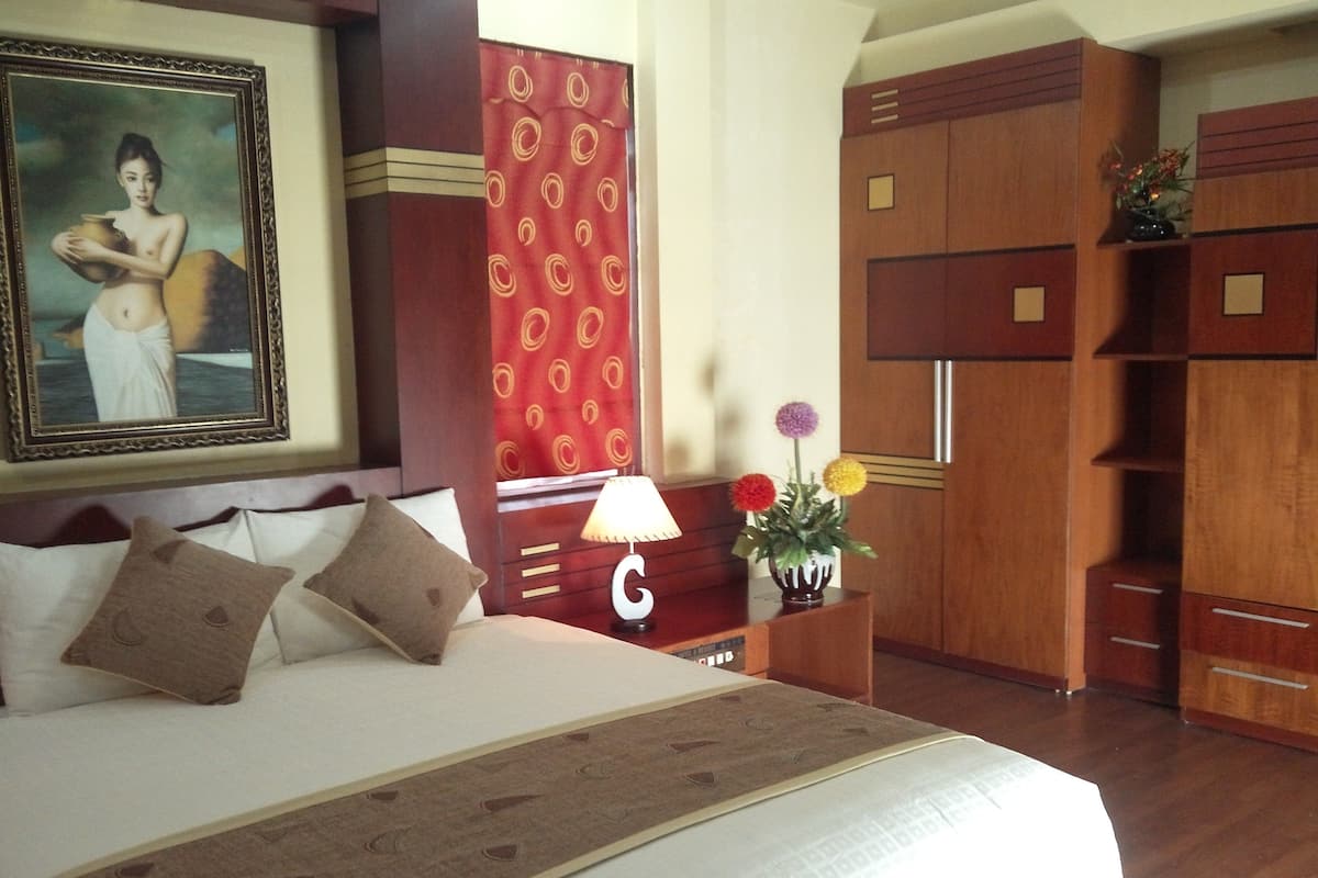 Une chambre d’hôtel avec un grand lit, une table de chevet avec une lampe, un vase de fleurs et un tableau au mur.